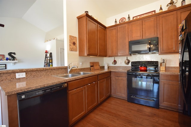 kitchen featuring brown cabinets, dark wood-type flooring, vaulted ceiling, black appliances, and a sink