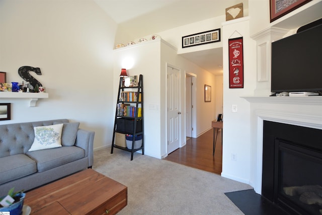 living area featuring vaulted ceiling, carpet floors, a fireplace with flush hearth, and baseboards