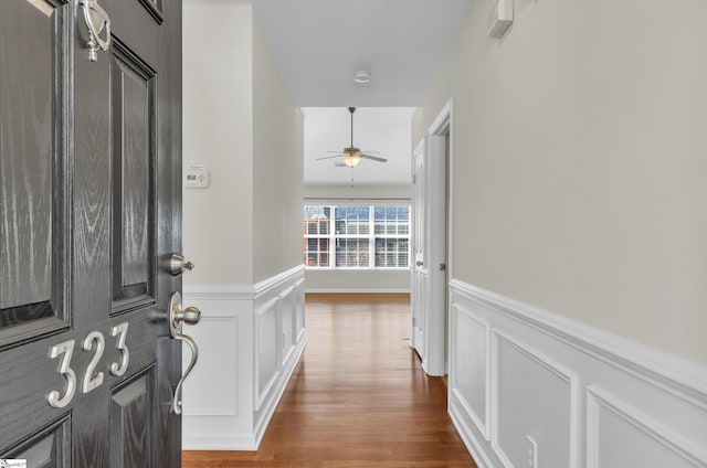 entrance foyer featuring a ceiling fan, wainscoting, a decorative wall, and wood finished floors