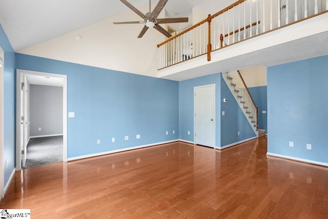 unfurnished room with baseboards, a ceiling fan, a towering ceiling, stairway, and wood finished floors