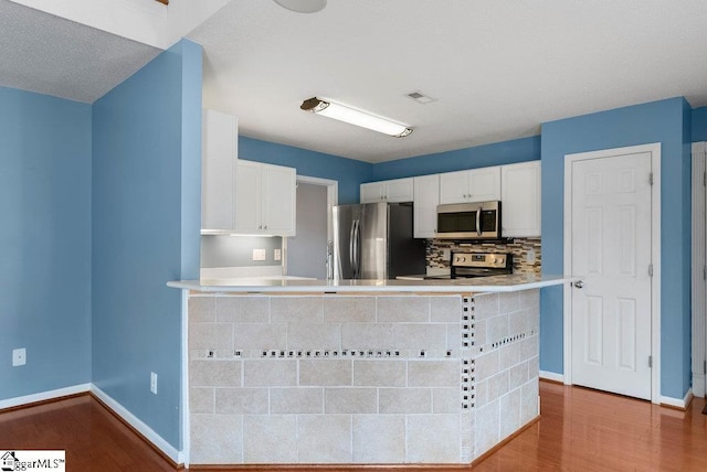 kitchen featuring stainless steel appliances, wood finished floors, visible vents, white cabinets, and backsplash