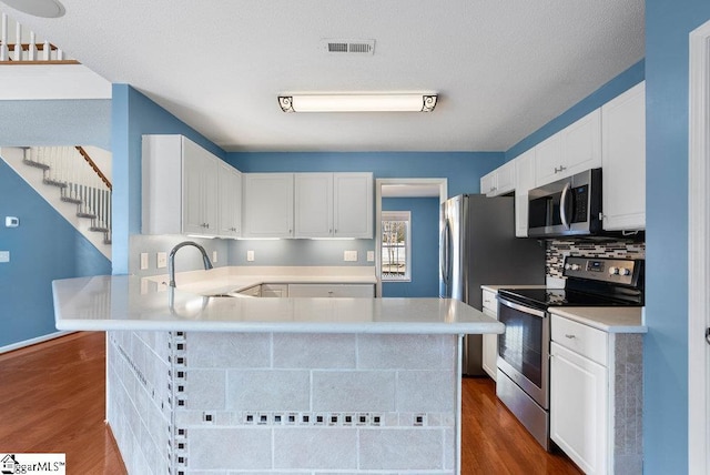 kitchen featuring stainless steel appliances, light countertops, visible vents, dark wood-type flooring, and a sink