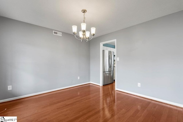 unfurnished room featuring a textured ceiling, a notable chandelier, wood finished floors, visible vents, and baseboards