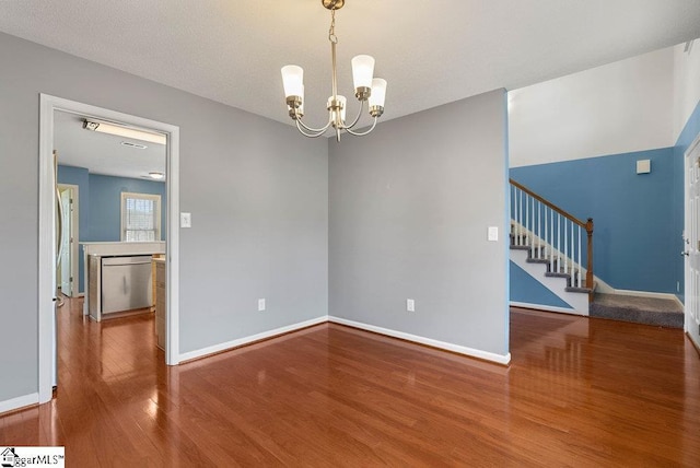 unfurnished room featuring stairs, a chandelier, wood finished floors, and baseboards