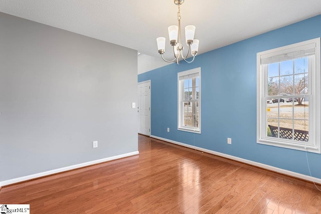 unfurnished room with a healthy amount of sunlight, an inviting chandelier, baseboards, and wood finished floors