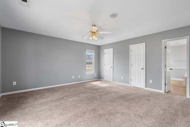 unfurnished bedroom featuring ceiling fan, visible vents, baseboards, multiple closets, and carpet