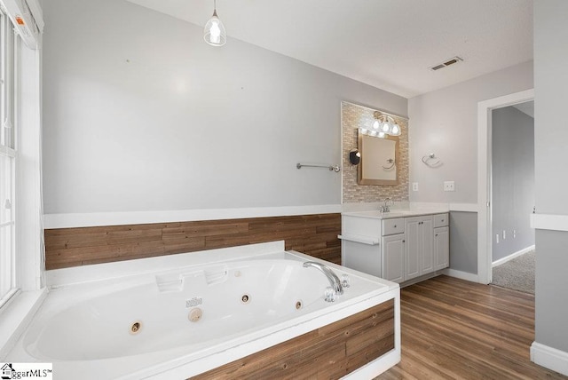 bathroom with a whirlpool tub, visible vents, wood finished floors, and vanity