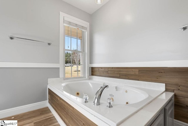 bathroom featuring lofted ceiling, a tub with jets, wood finished floors, and baseboards