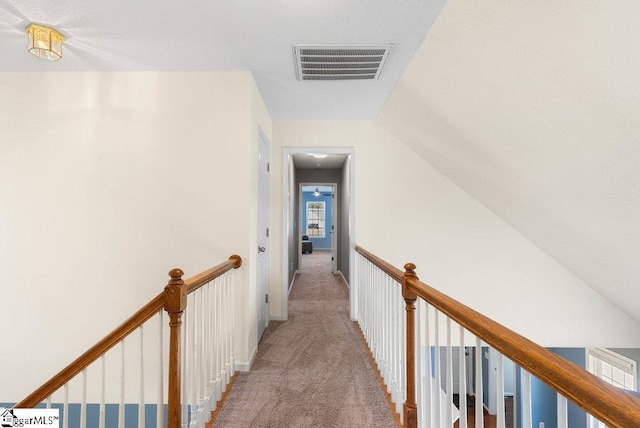 hallway with lofted ceiling, an upstairs landing, visible vents, and light colored carpet