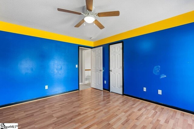 spare room with a ceiling fan, a textured ceiling, baseboards, and wood finished floors