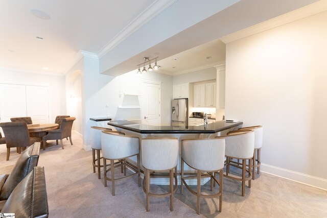 kitchen featuring a breakfast bar area, dark countertops, stainless steel fridge with ice dispenser, ornamental molding, and baseboards