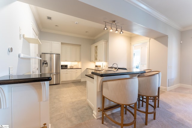 kitchen with stainless steel fridge, visible vents, dark countertops, ornamental molding, and a peninsula