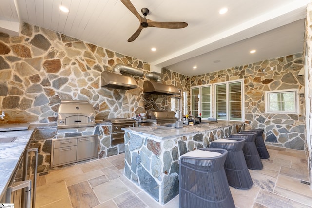 kitchen with beam ceiling, stone tile floors, wall chimney exhaust hood, and light stone countertops