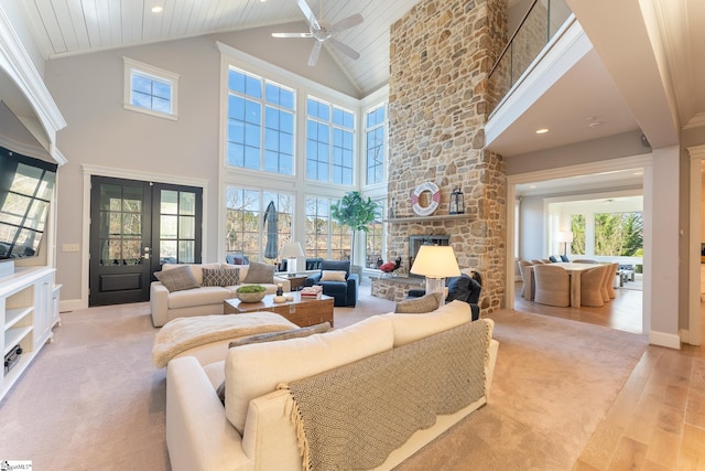 living room with high vaulted ceiling, a stone fireplace, baseboards, french doors, and light wood-type flooring