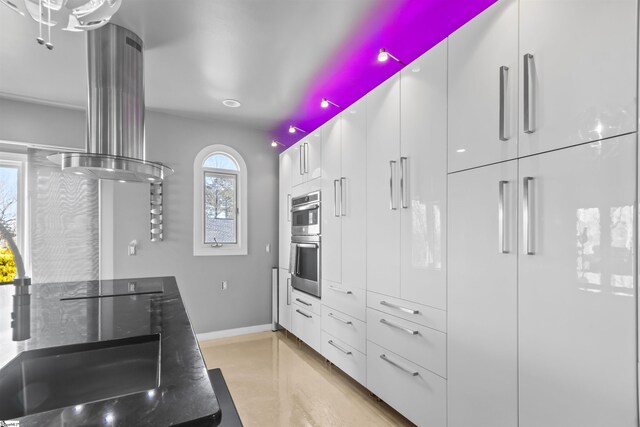 kitchen with baseboards, island range hood, modern cabinets, stainless steel double oven, and white cabinetry