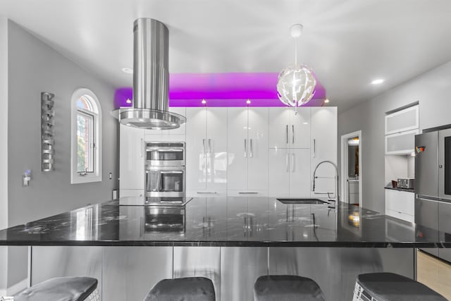 kitchen featuring a breakfast bar, island exhaust hood, stainless steel appliances, hanging light fixtures, and a sink