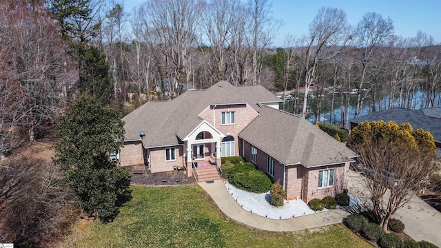 view of front of home featuring a forest view, brick siding, a shingled roof, and a front lawn