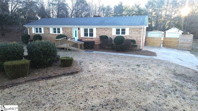 single story home with a chimney, an outbuilding, concrete driveway, and brick siding