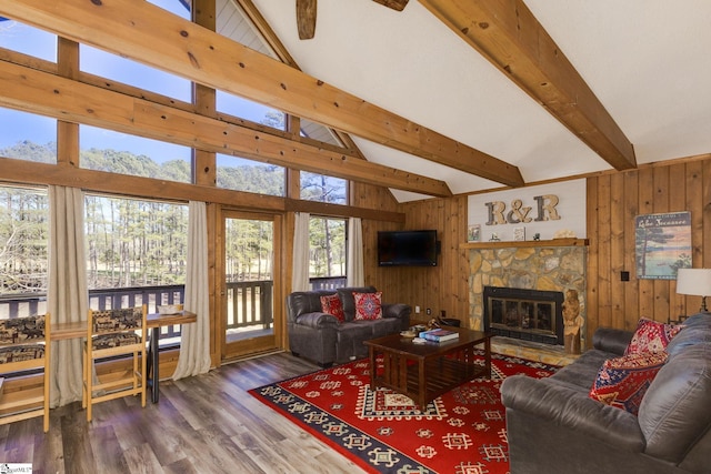 living area featuring wood walls, a stone fireplace, beamed ceiling, and wood finished floors