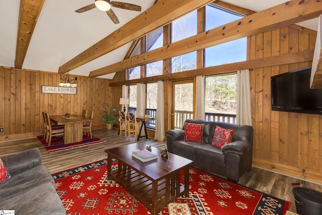 living area with beam ceiling, a ceiling fan, wood walls, wood finished floors, and baseboards