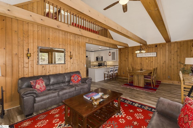 living area featuring wooden walls, a ceiling fan, beam ceiling, and wood finished floors