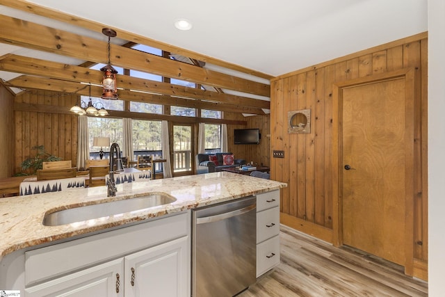 kitchen featuring a sink, wood walls, dishwasher, and hanging light fixtures