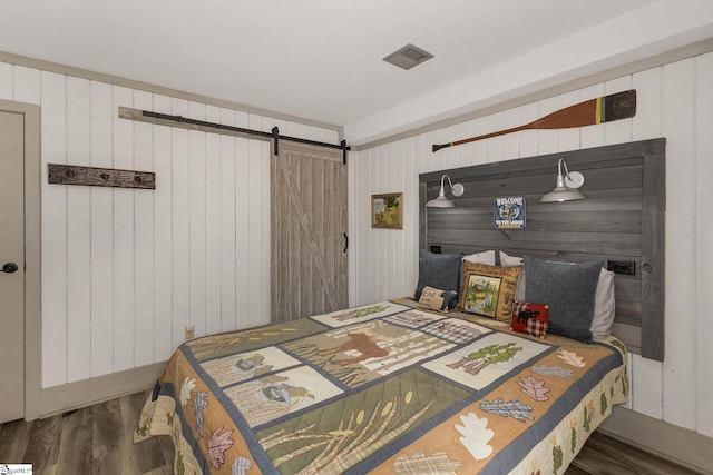 bedroom with a barn door, visible vents, and wood finished floors