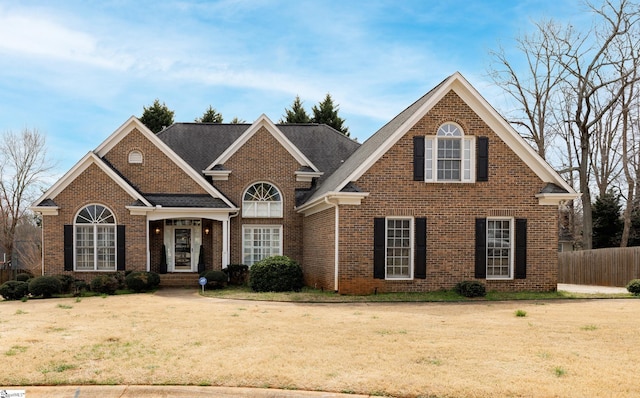 traditional-style home with a front yard, fence, and brick siding