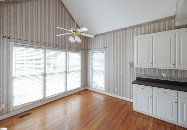 unfurnished dining area featuring light wood-style floors, visible vents, vaulted ceiling, and wallpapered walls