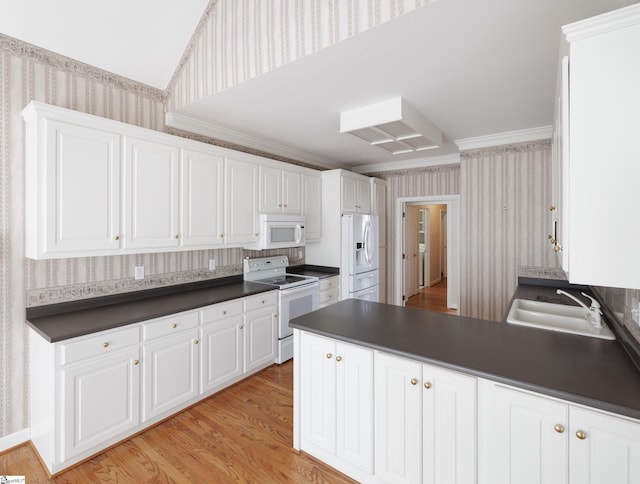 kitchen with dark countertops, white appliances, a sink, and wallpapered walls