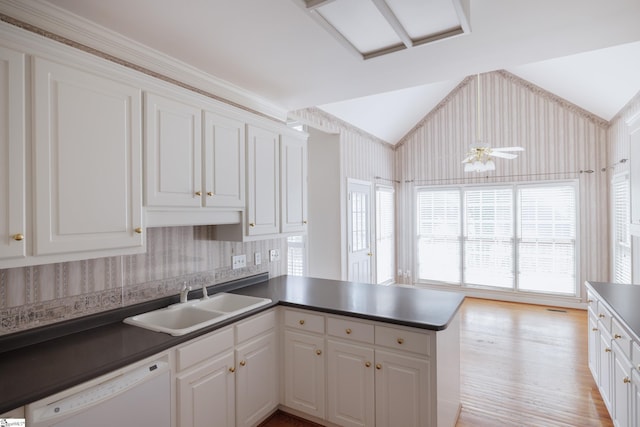 kitchen featuring dishwasher, a peninsula, dark countertops, and a sink