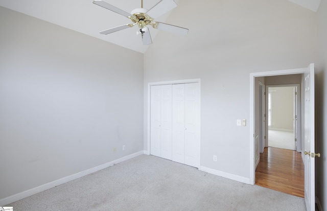 unfurnished bedroom featuring a closet, a ceiling fan, carpet flooring, high vaulted ceiling, and baseboards