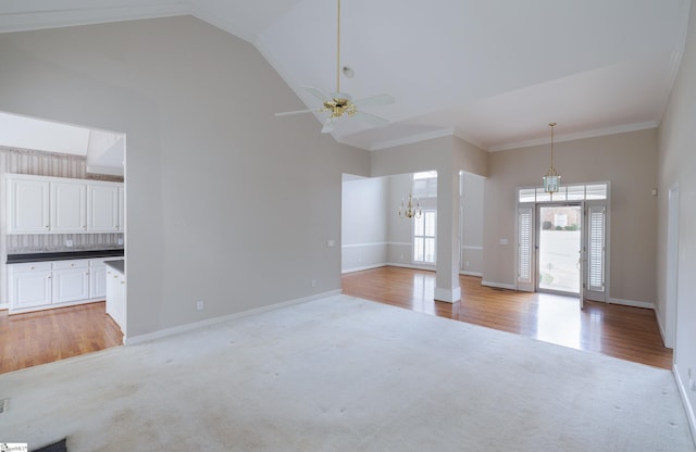 unfurnished living room featuring baseboards, high vaulted ceiling, ornamental molding, and light colored carpet