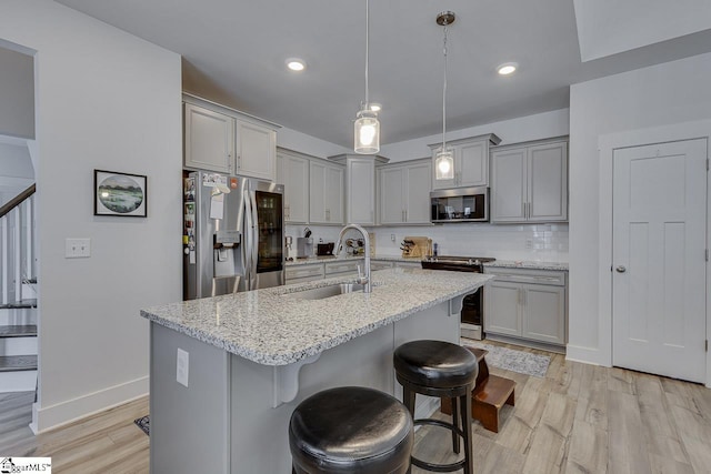 kitchen with a sink, stainless steel appliances, gray cabinetry, a kitchen bar, and backsplash