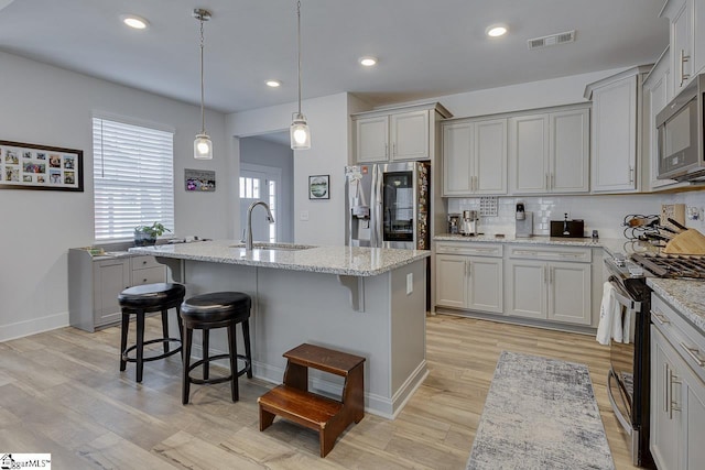 kitchen featuring tasteful backsplash, visible vents, appliances with stainless steel finishes, a sink, and a kitchen breakfast bar