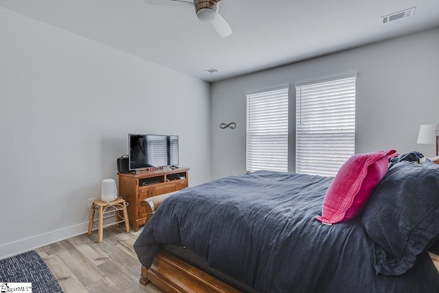 bedroom with a ceiling fan, visible vents, baseboards, and wood finished floors