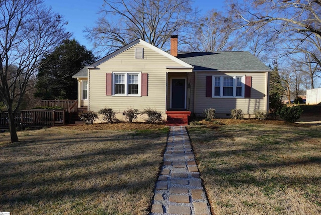 view of front of property with a shingled roof, a front lawn, and a chimney