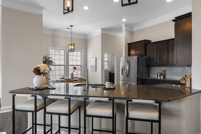 kitchen featuring ornamental molding, a sink, dark brown cabinets, stainless steel refrigerator with ice dispenser, and tasteful backsplash