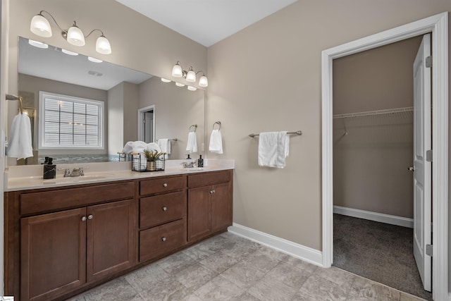 bathroom with double vanity, a spacious closet, baseboards, and a sink