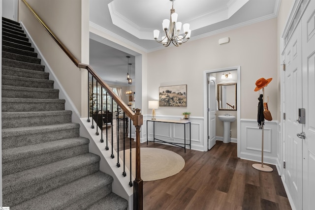 interior space featuring a notable chandelier, ornamental molding, wood finished floors, wainscoting, and a raised ceiling