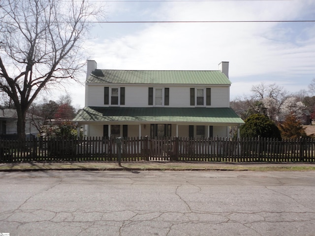 view of front facade featuring metal roof, a fenced front yard, a chimney, and a porch