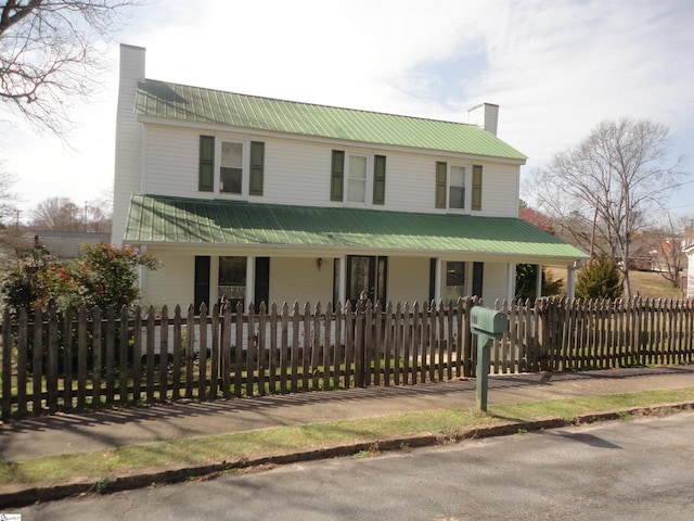 view of front of home with a porch, metal roof, a chimney, and a fenced front yard