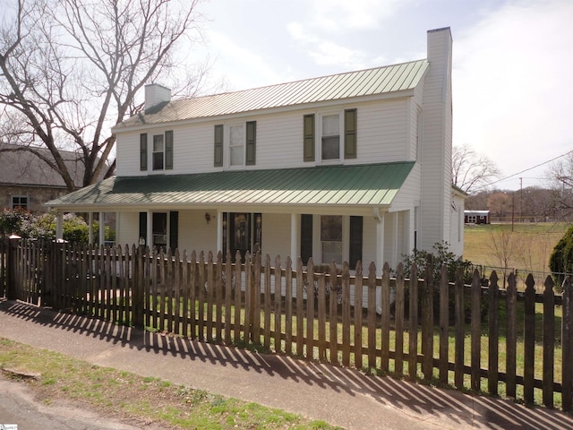 farmhouse-style home with metal roof, a porch, a chimney, and a fenced front yard