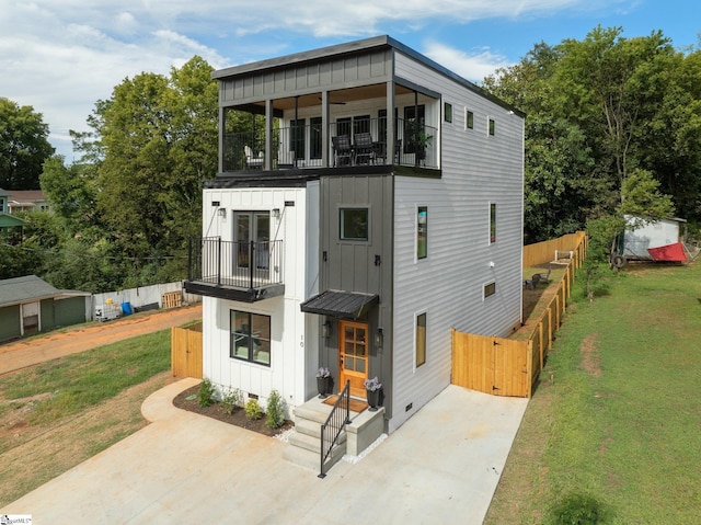 modern home with a balcony, fence, french doors, a front lawn, and board and batten siding