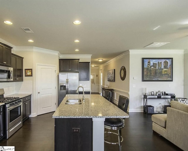 kitchen featuring visible vents, a kitchen island with sink, a sink, stainless steel appliances, and light stone countertops