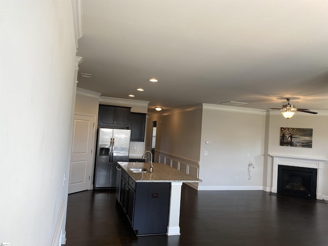 kitchen featuring light stone counters, a fireplace with flush hearth, ornamental molding, a sink, and stainless steel refrigerator with ice dispenser