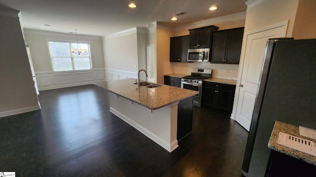 kitchen featuring a sink, stainless steel appliances, wainscoting, light stone countertops, and dark wood-style flooring