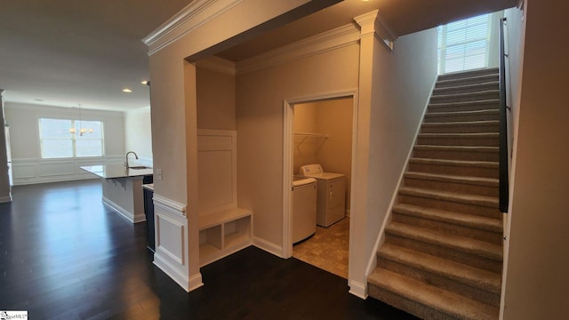 staircase with a decorative wall, wood finished floors, ornamental molding, and washing machine and clothes dryer