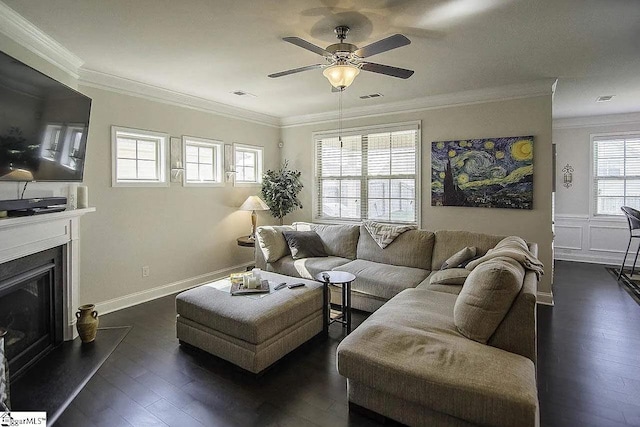 living area with visible vents, dark wood-style flooring, crown molding, and a glass covered fireplace