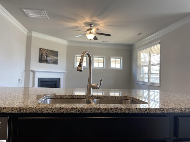 kitchen with a fireplace, light stone countertops, crown molding, and a sink